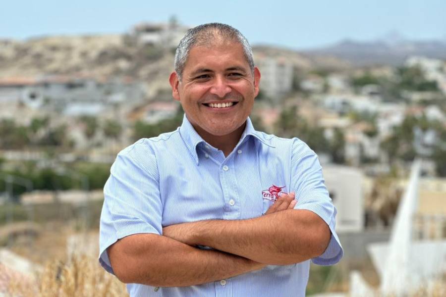 Primer plano de un hombre sonriente con una camisa azul y los brazos cruzados.