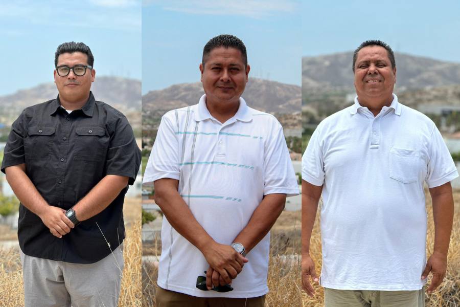 Tres hombres sonrientes, uno al lado del otro, de pie frente a una montaña.